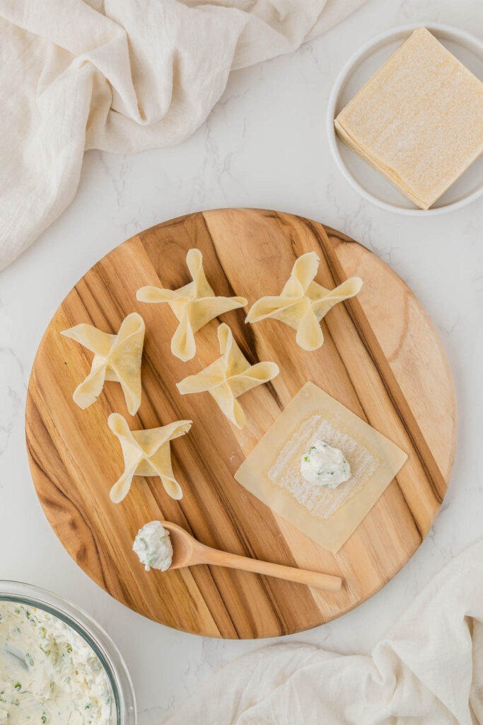 cream cheese rangoon filling on spoon, wonton wrapper and Panda Express rangoon folded on wooden circle platter