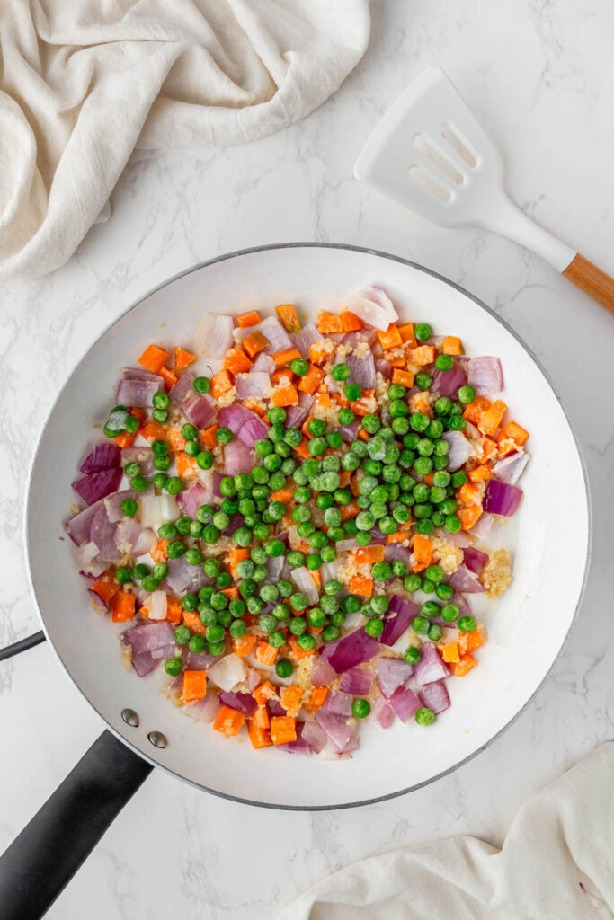 carrots red onion and peas cooking in white pan