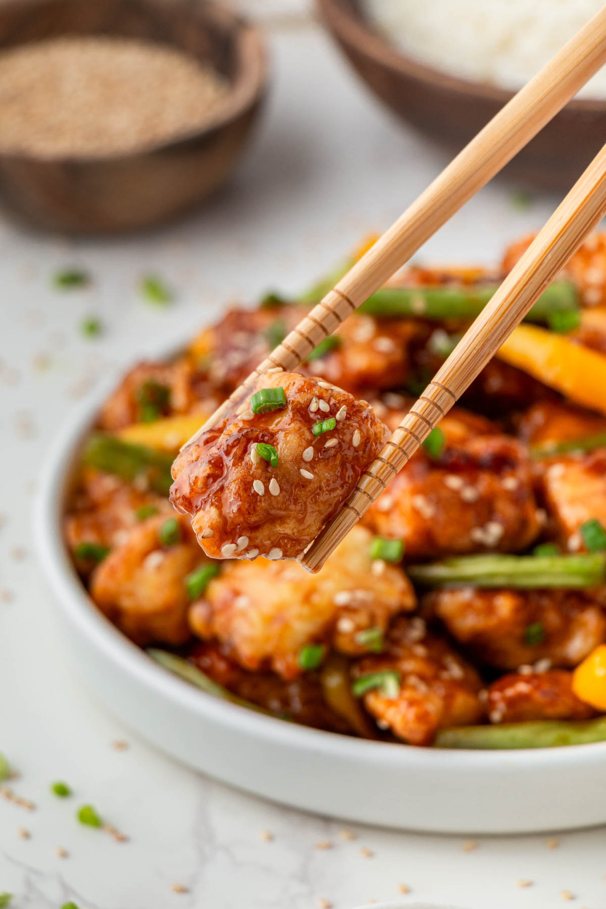 close up of white bowl of Panda Express Sesame Chicken with peppers and green beans in chop sticks