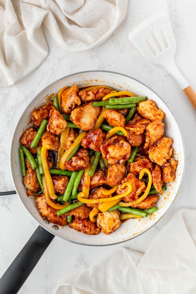 Panda Express honey sesame chicken recipe cooked in a skillet with green beans and yellow bell peppers