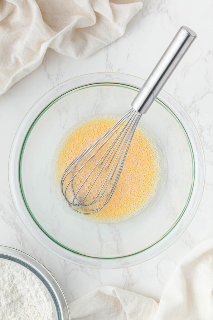 egg mixture in clear bowl with stainless steel whisk