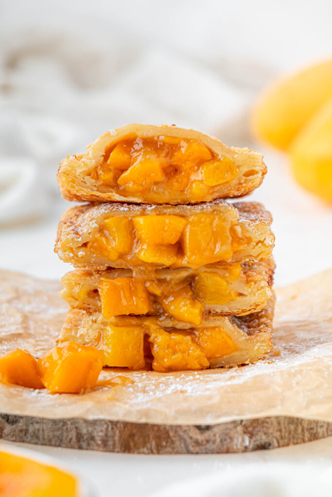 side view of stacked Jollibee peach mango pies cut in half on parchment paper covered serving board