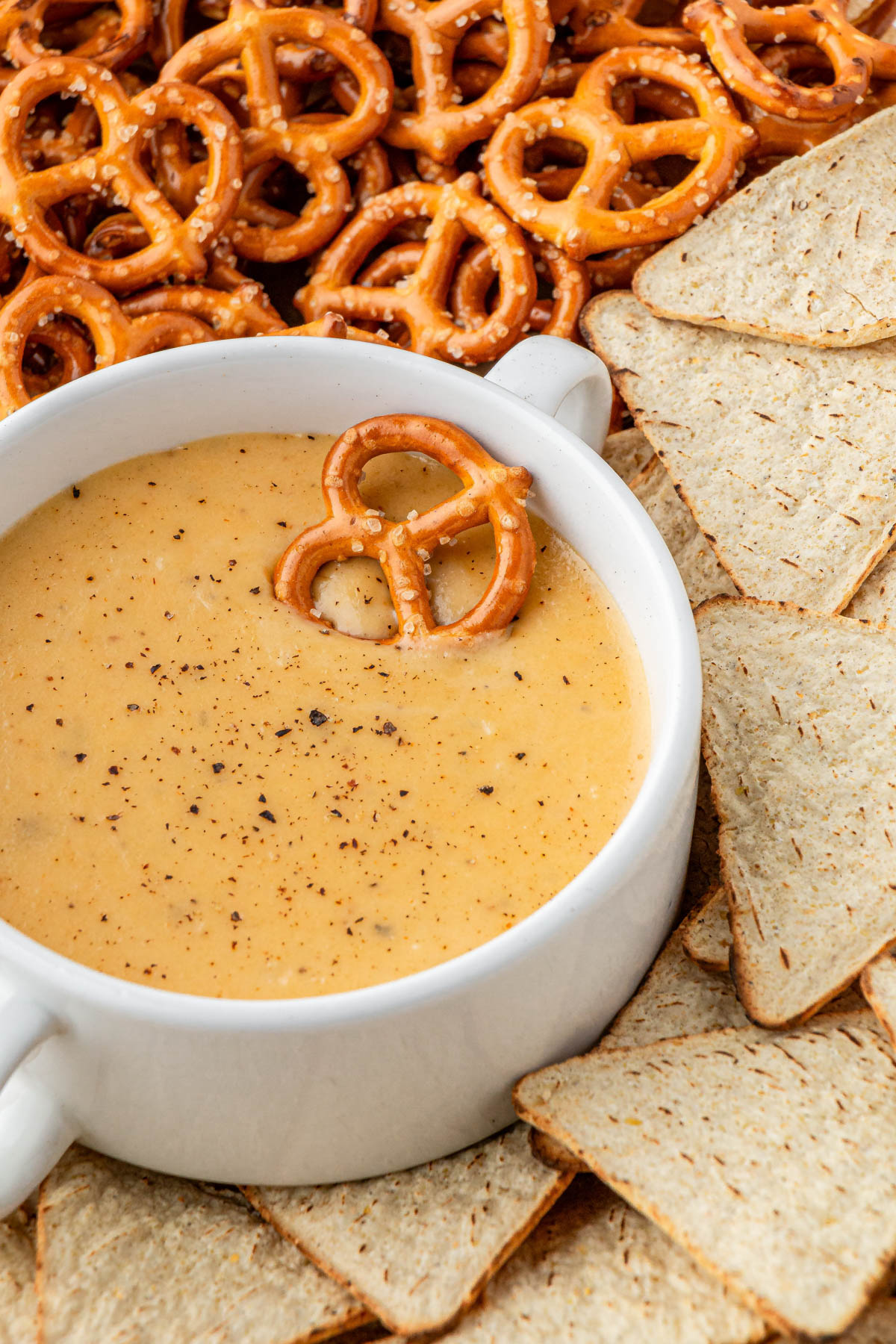 overhead view of Applebees beer cheese dip in white bowl with pretzel on top and pretzels and chips around it