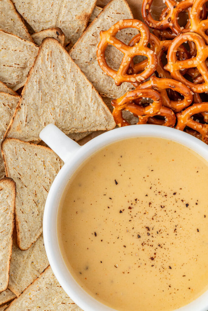 close up of Applebees beer cheese dip in white bowl with pretzels and chips around it