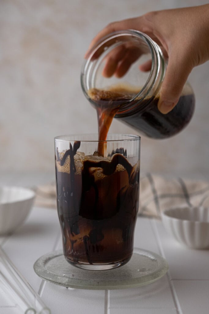 Pouring chilled brewed coffee over ice into chocolate-drizzled glass