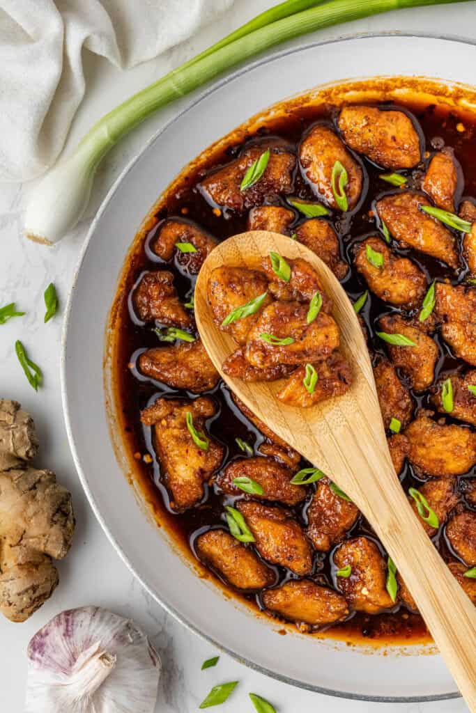 Close up of glazed bourbon chicken on wooden spoon