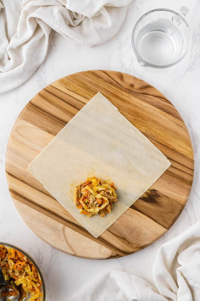 overhead view of egg roll filling on egg roll wrapper on wooden platter