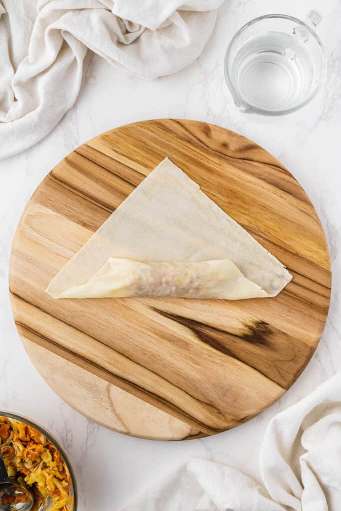 overhead view egg roll getting wrapped on wooden platter