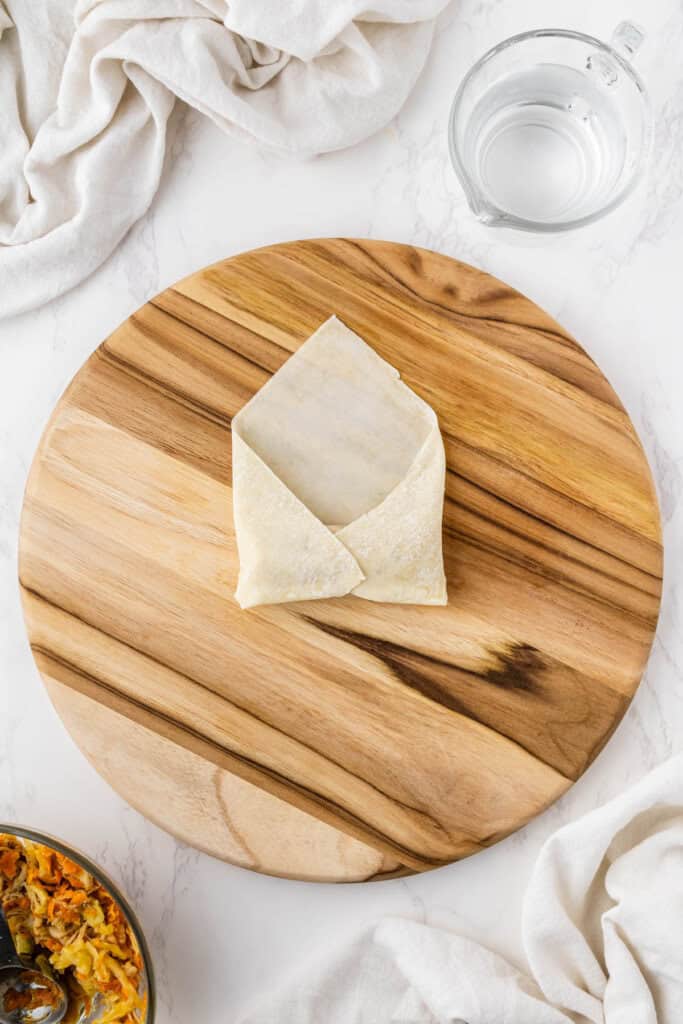 overhead view egg roll getting wrapped on wooden platter