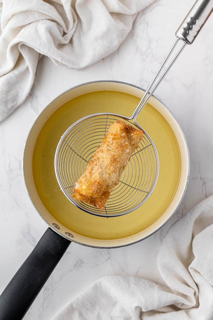 overhead view of cooked panda express chicken egg roll getting taken out of hot oil with wire spoon