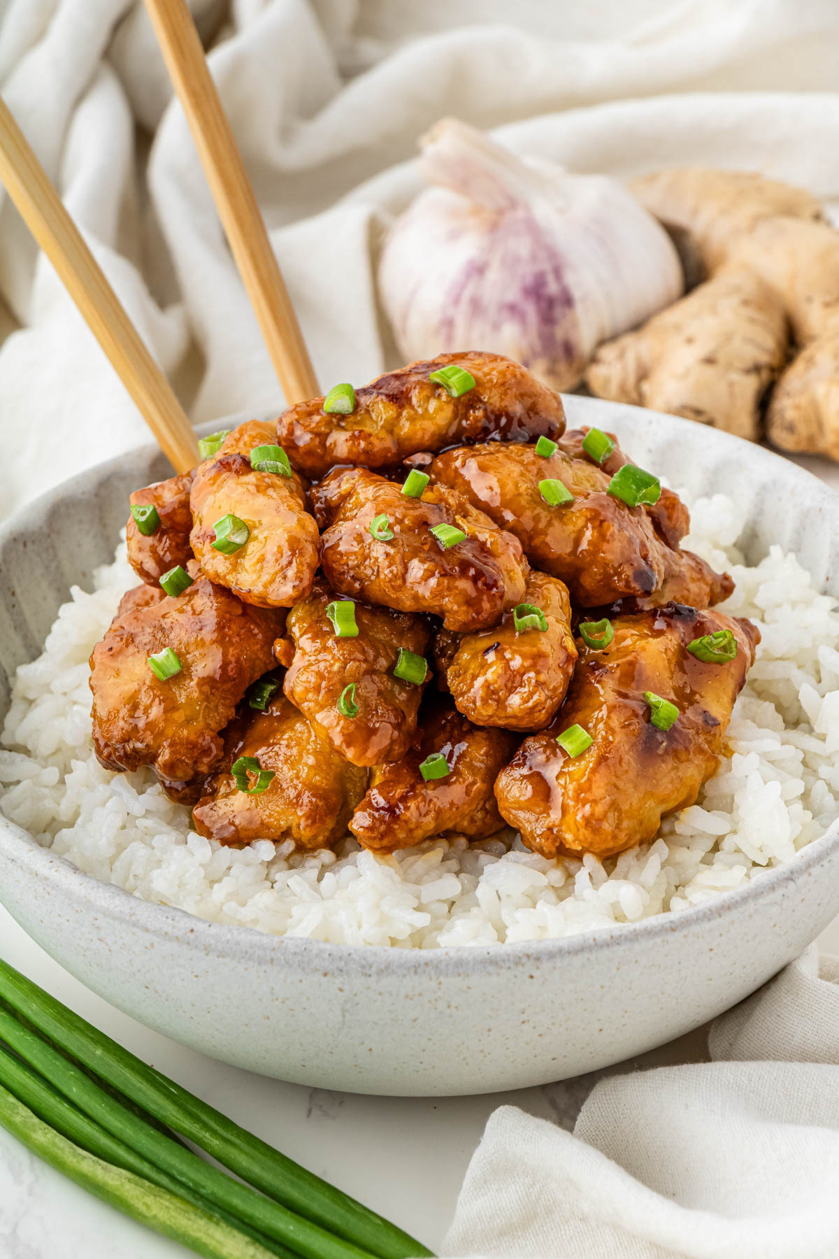 Orange Chicken on top of a bed of rice in a grey bowl with chop sticks