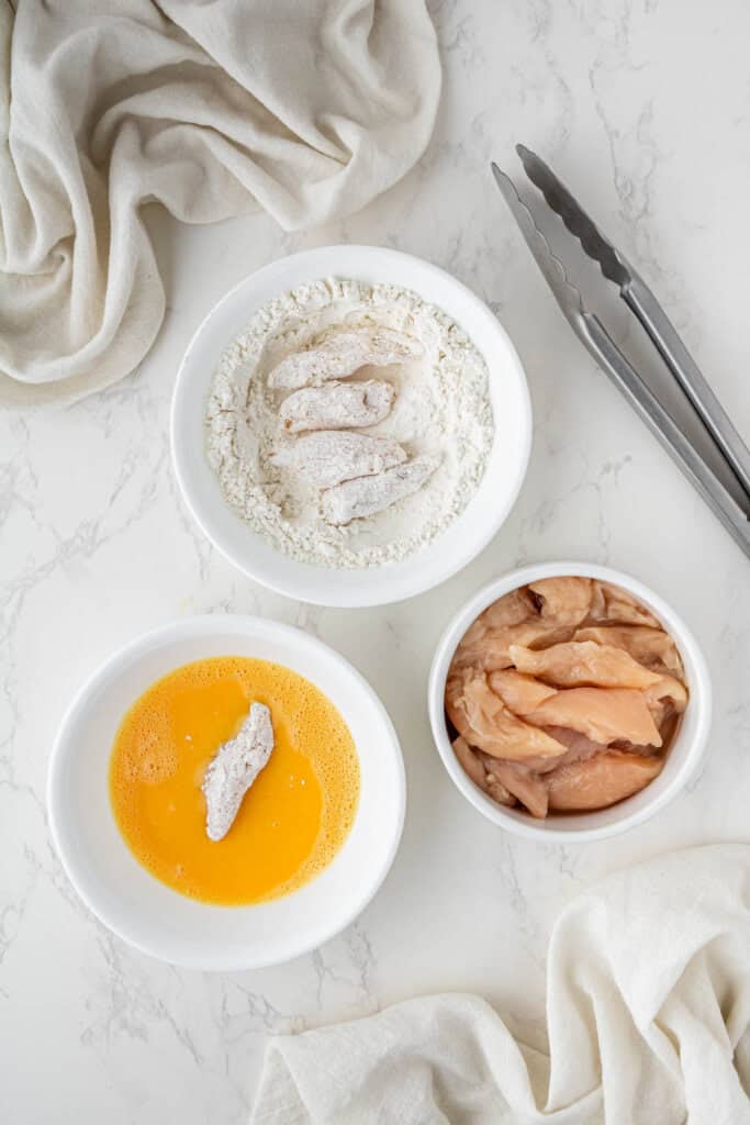 overhead view of chicken, eggs and flour in bowls
