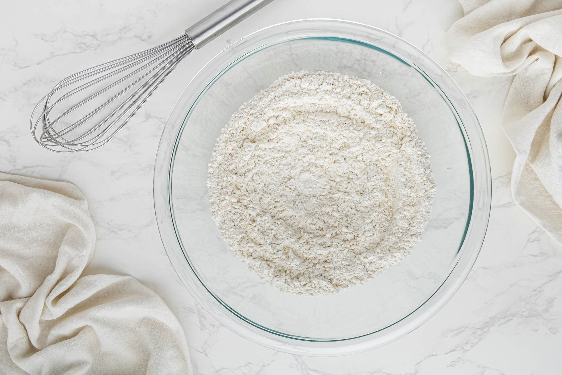 flour and dry ingredients in clear bowl with whisk
