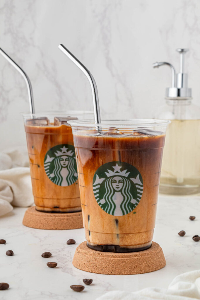 two starbucks Iced Shaken Espresso drinks on wood coaster with milk on with metal straws and coffee beans on counter