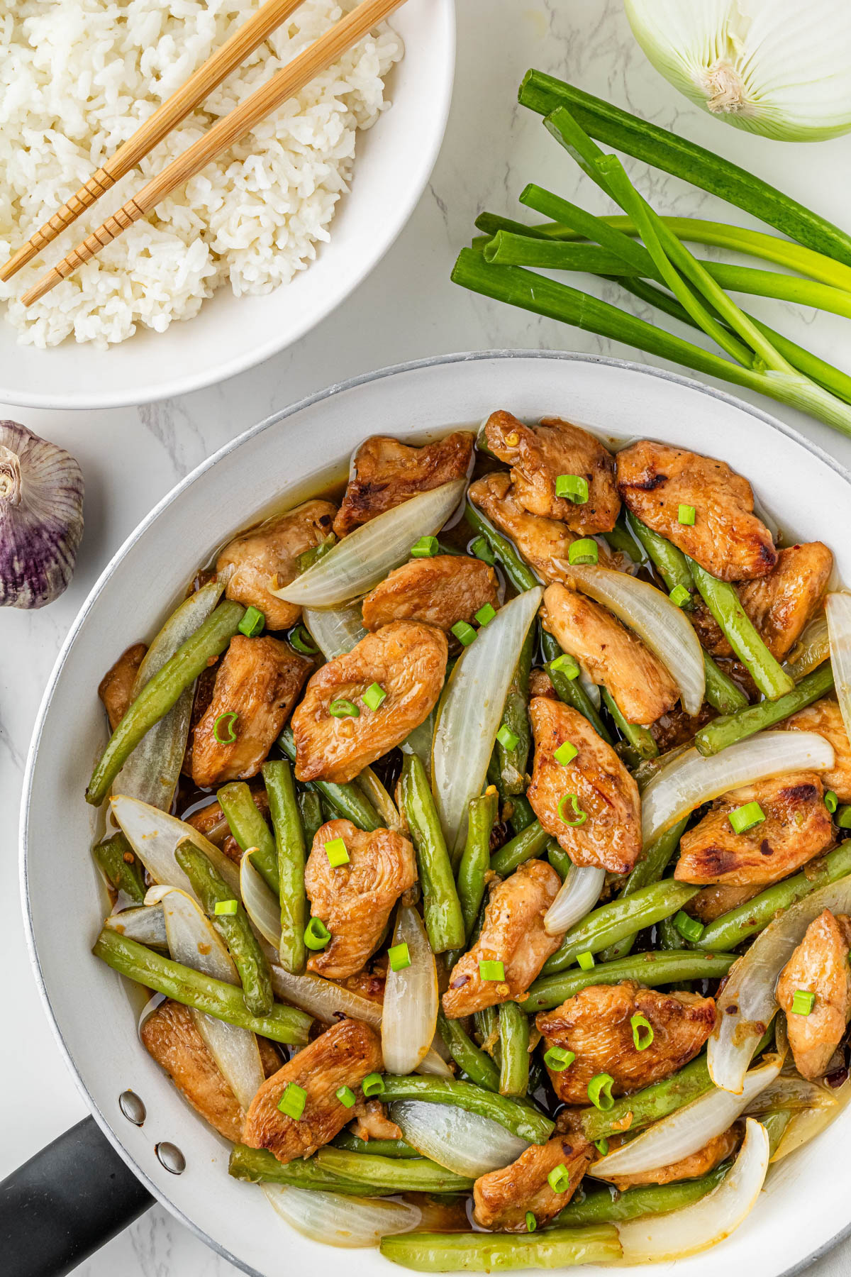 overhead view of Panda Express String Bean Chicken in a pan with green onions and white rice in the background