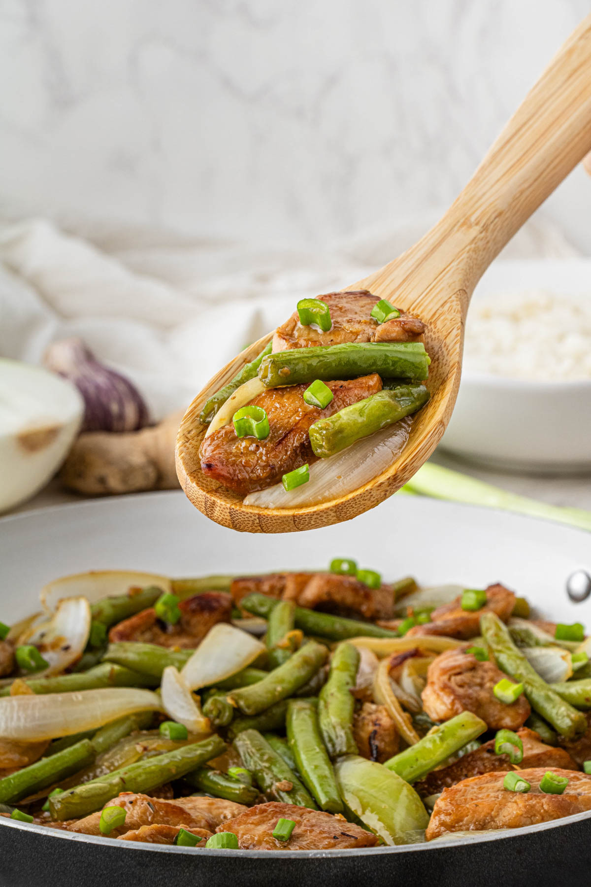 Panda Express String Bean Chicken in a pan with green onions with a wooden spoon holding some in the air