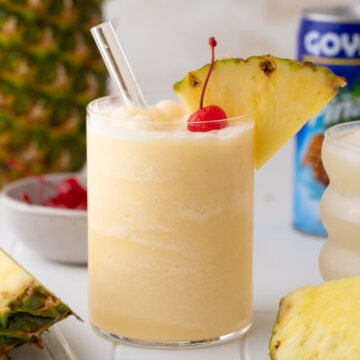 topical Goya Pina colada with pineapple wedge and cherry with pineapple and coconut in the background