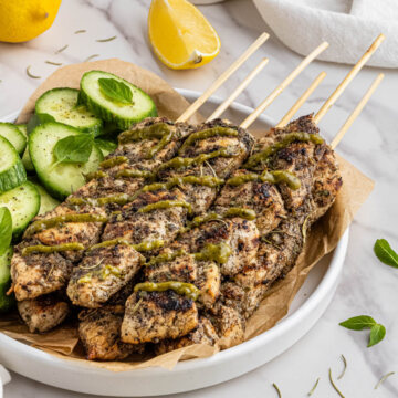 costco chicken skewers recipe on white plate with side of cucumber and green sauce on top