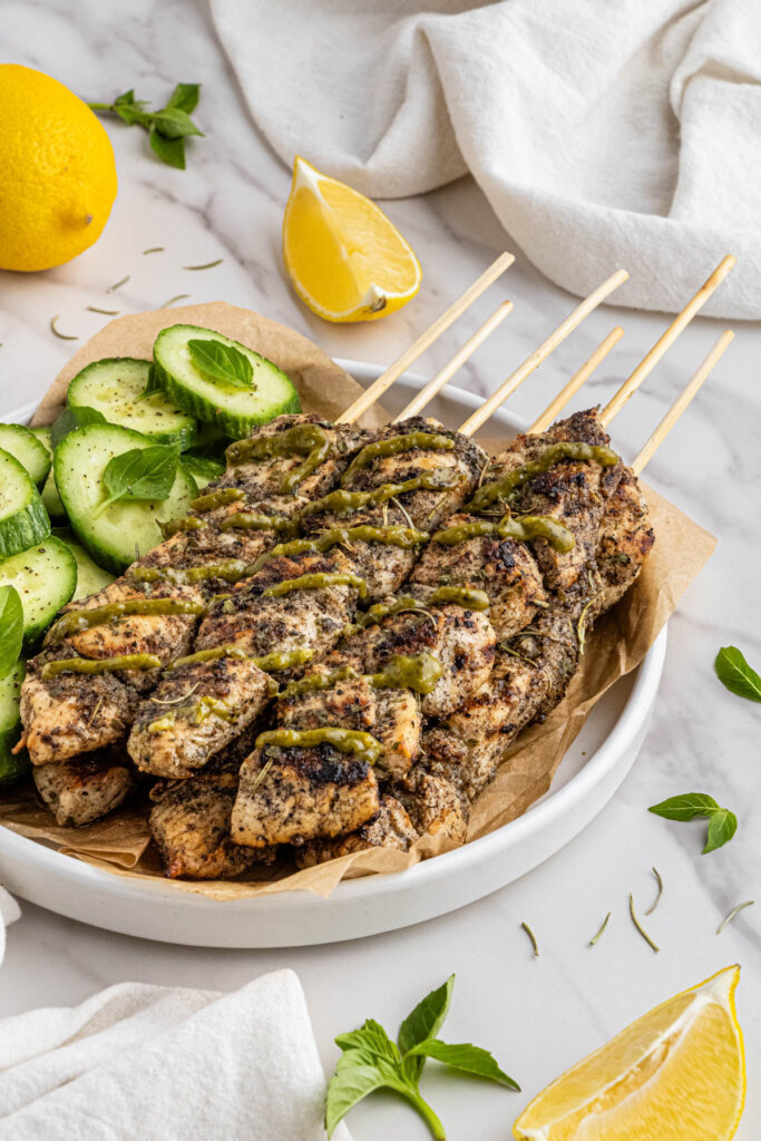 costco chicken skewers recipe on white plate with side of cucumber and green sauce on top