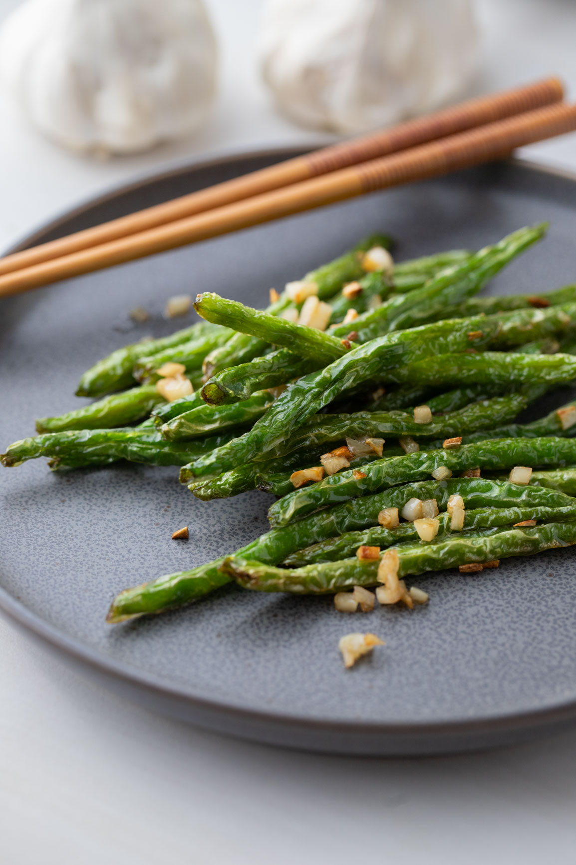 Din Tai Fung Green Beans with garlic on a black plate with a wooden chopsticks