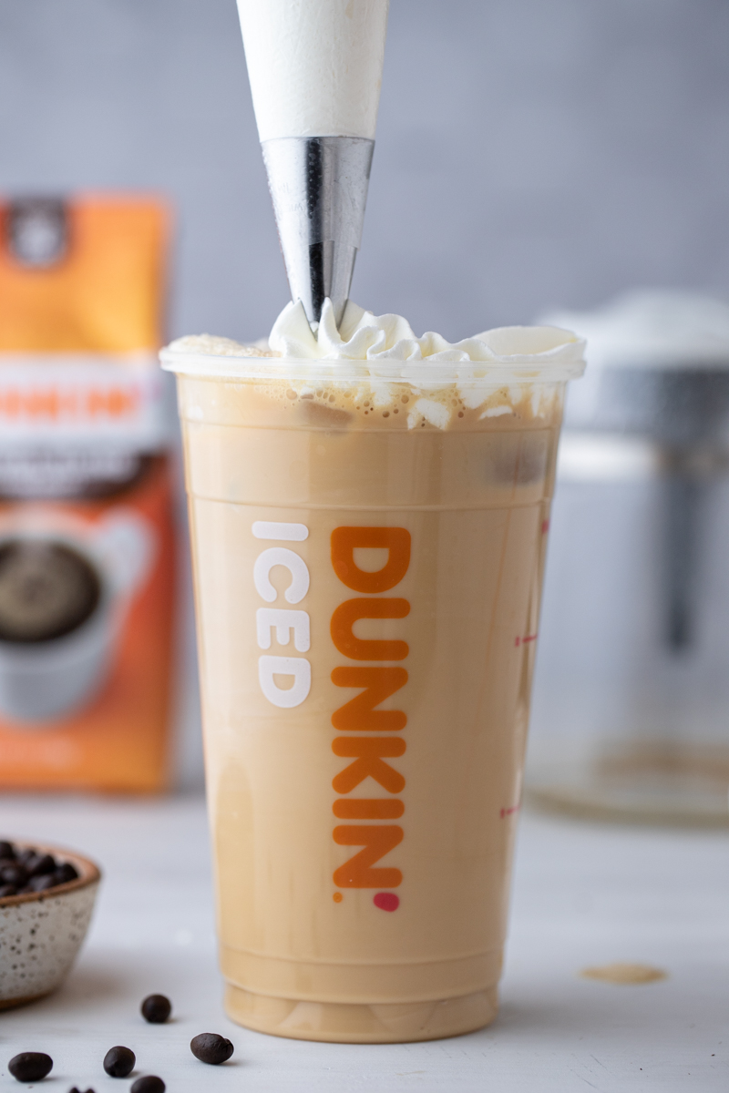 whipped cream being poured over the dunkin donuts iced coffee recipe