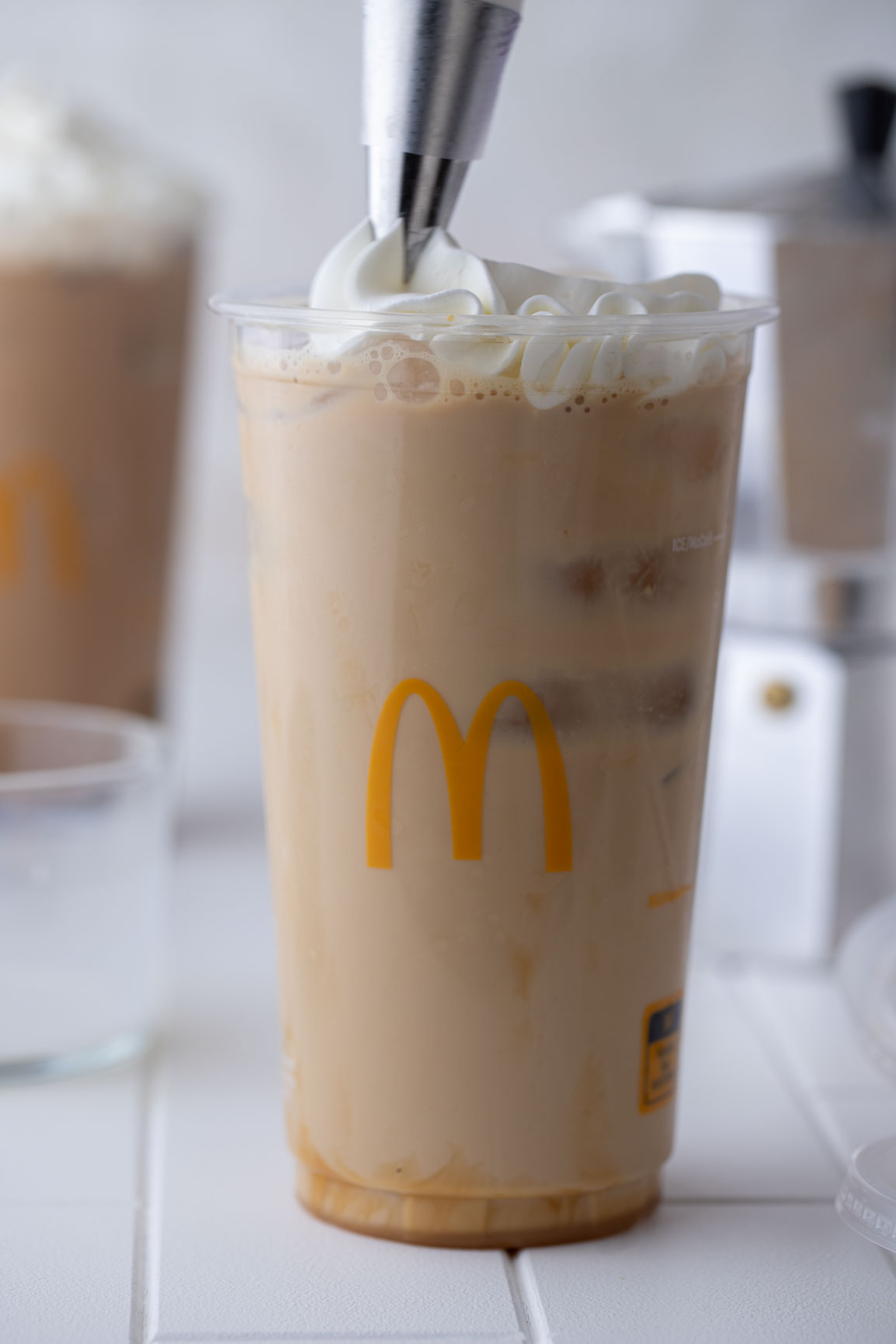 the cup of mcdonald's caramel iced coffee being topped with whipped cream