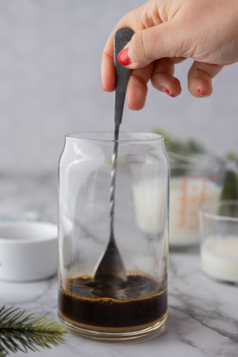 a hand stirring a spoon into espresso and white chocolate sauce