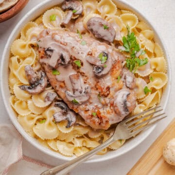 overhead view of copycat Cheesecake Factory Chicken Marsala on pasta with parsley and mushrooms with a white bowl with fork