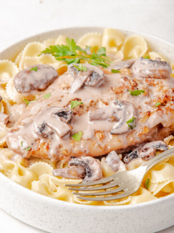 overhead view of copycat Cheesecake Factory Chicken Marsala on pasta with parsley and mushrooms with a white bowl with fork