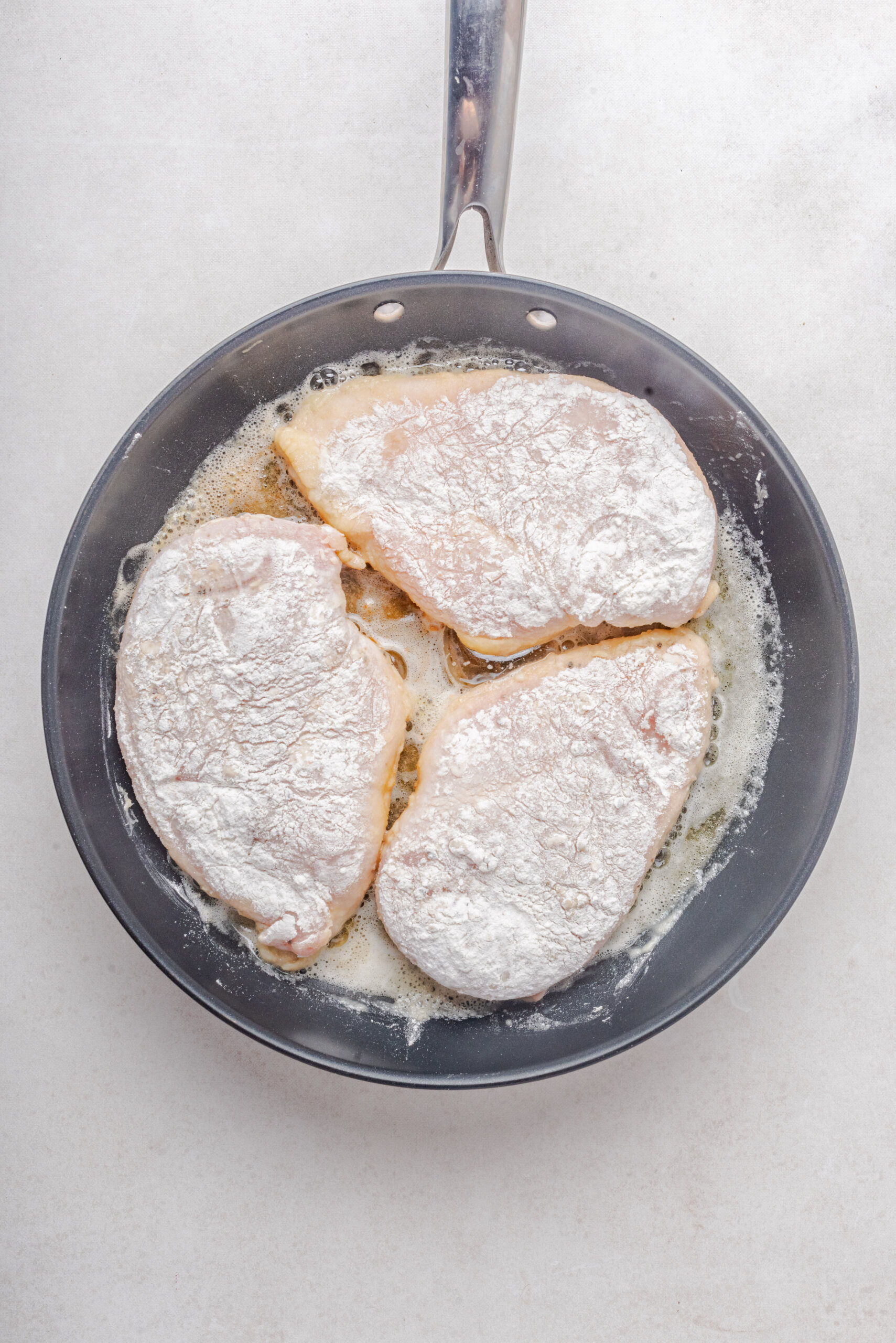 three chicken breasts in skillet cooking