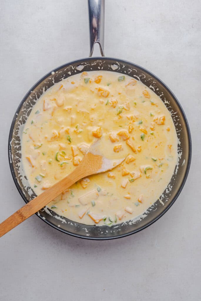 Cheese and cream mixture beginning to melt in a skillet, stirred with a wooden spoon.