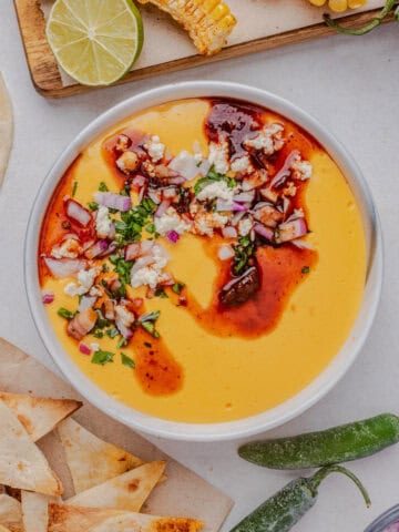 Overhead bowl of Torchy's Queso recipe topped with salsa, cilantro, cotija cheese, and diced onions.