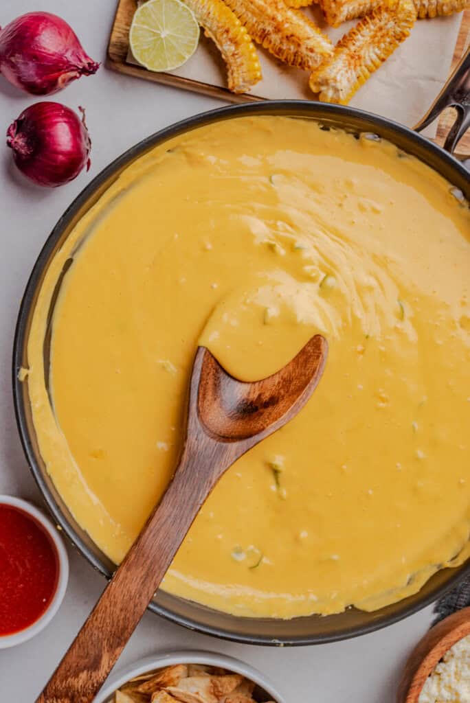 Fully melted queso in a skillet with a wooden spoon resting inside.
