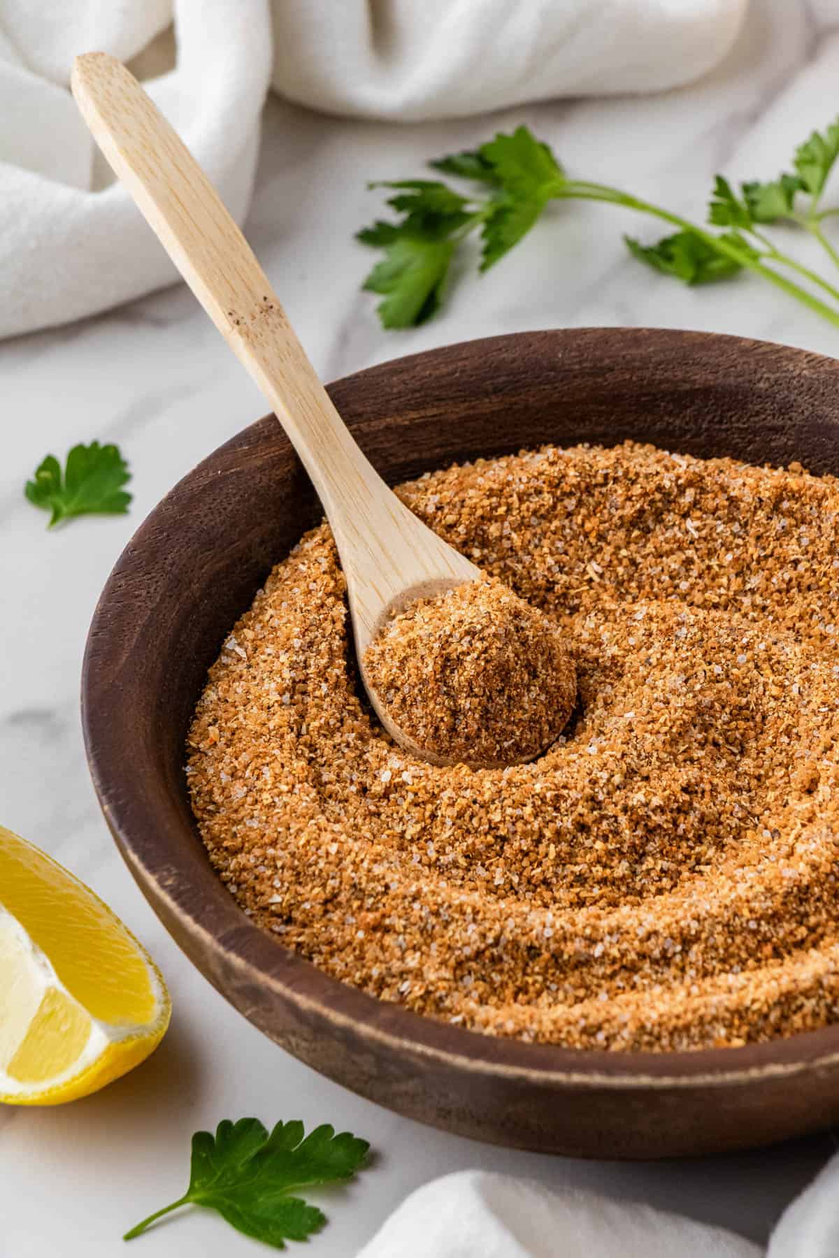 copycat Buffalo Wild Wings dry rub recipe in brown bowl with lemon and fresh herbs in the background with wooden spoon