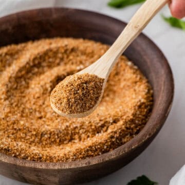 copycat Buffalo Wild Wings dry rub recipe in brown bowl with lemon and fresh herbs in the background with wooden spoon
