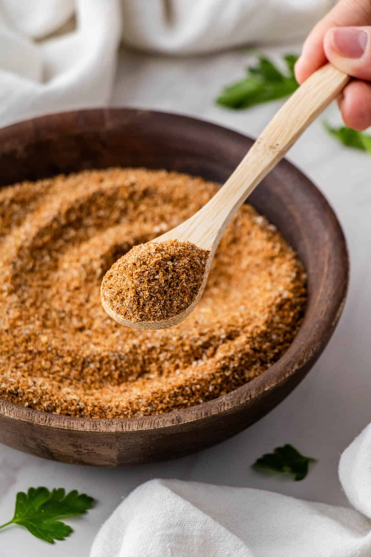 copycat Buffalo Wild Wings dry rub recipe in brown bowl with lemon and fresh herbs in the background with wooden spoon
