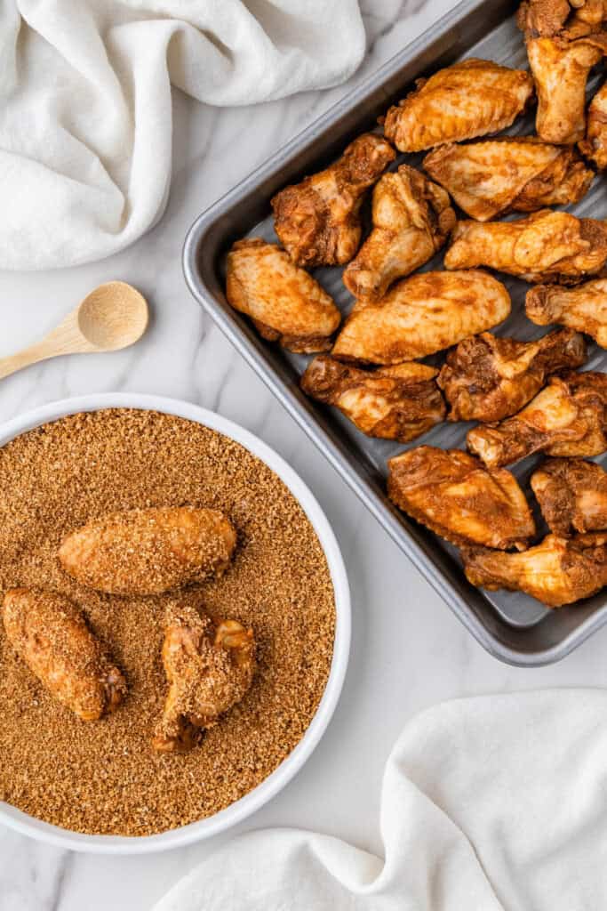copycat Buffalo Wild Wings dry rub on chicken on baking sheet and three in seasoning mixture in white bowl