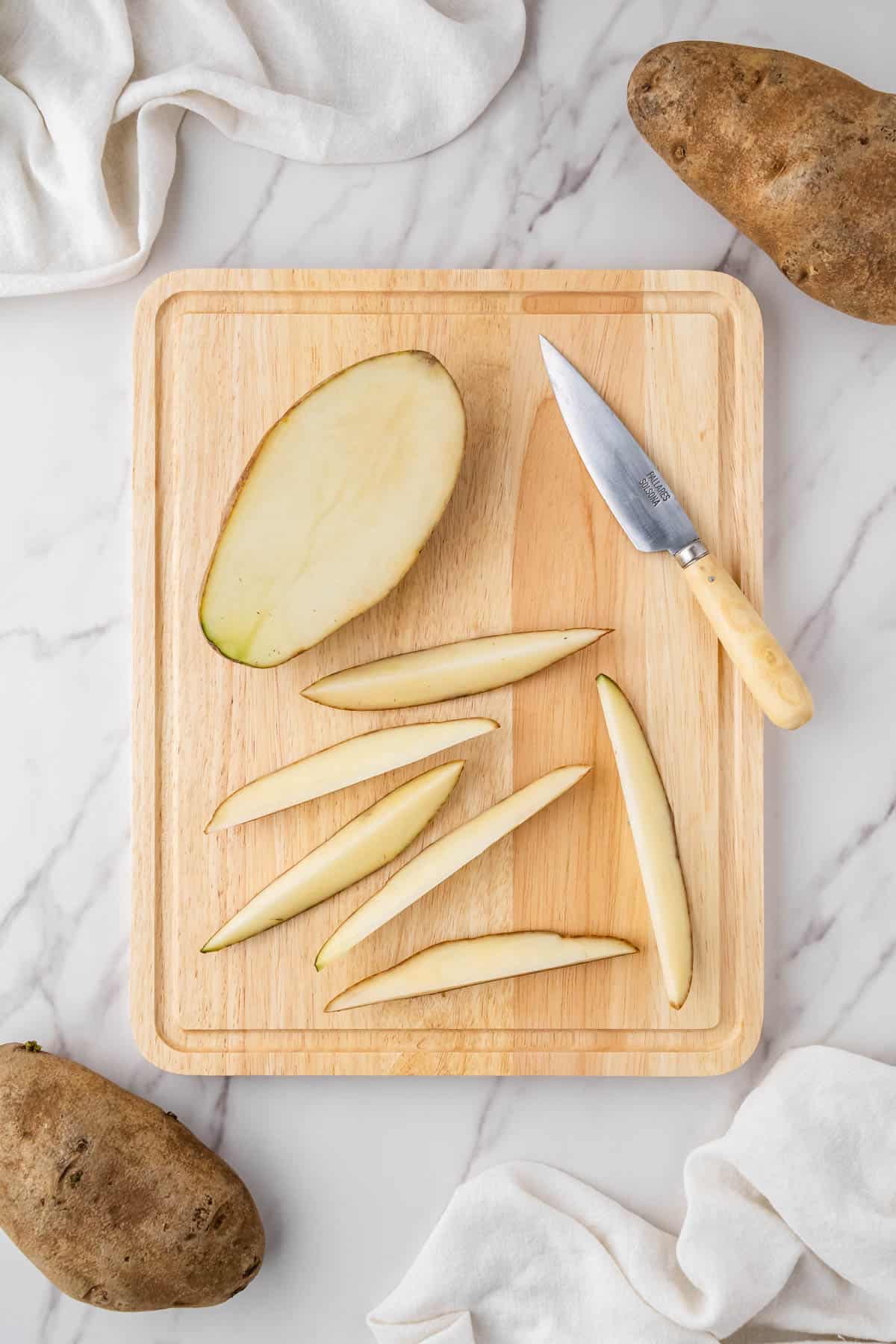 russet potatoes being cut into wedges on wooden cutting board