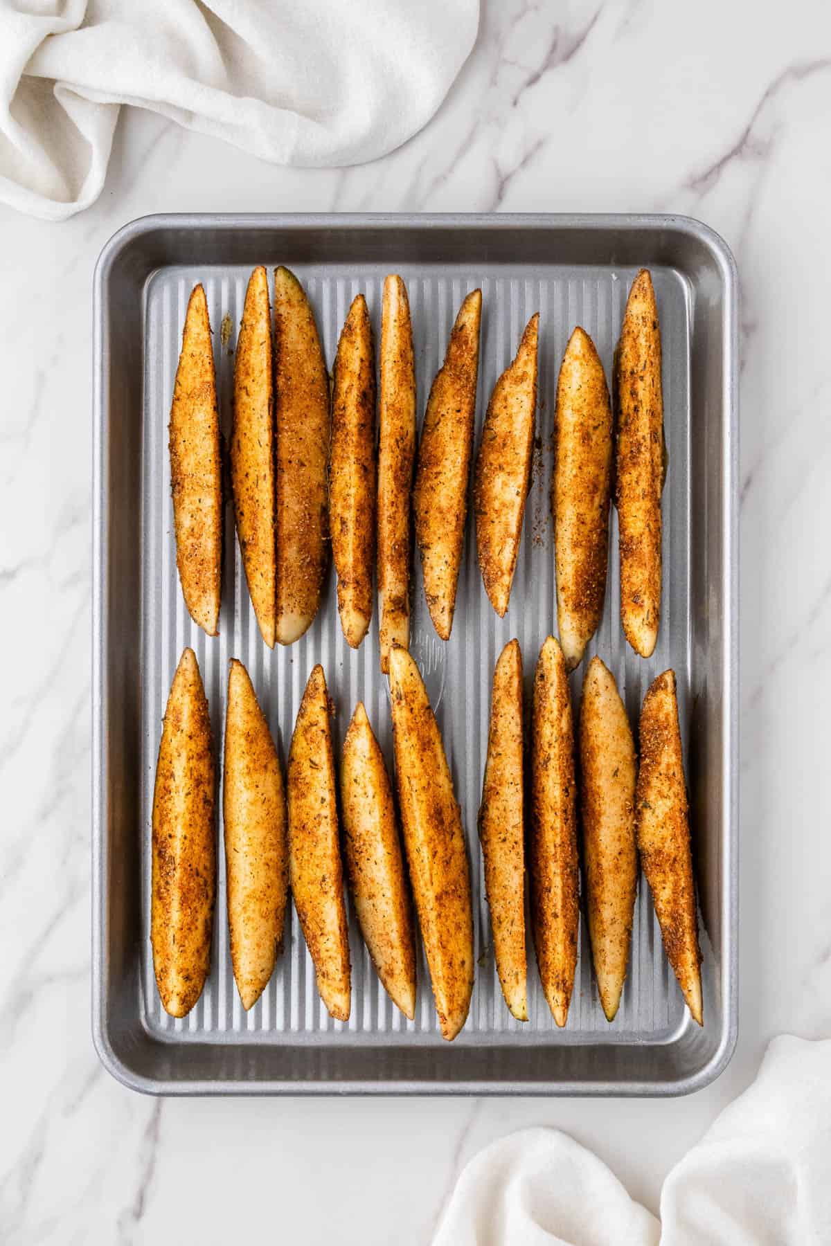 raw potato wedges with seasoning with baking sheet
