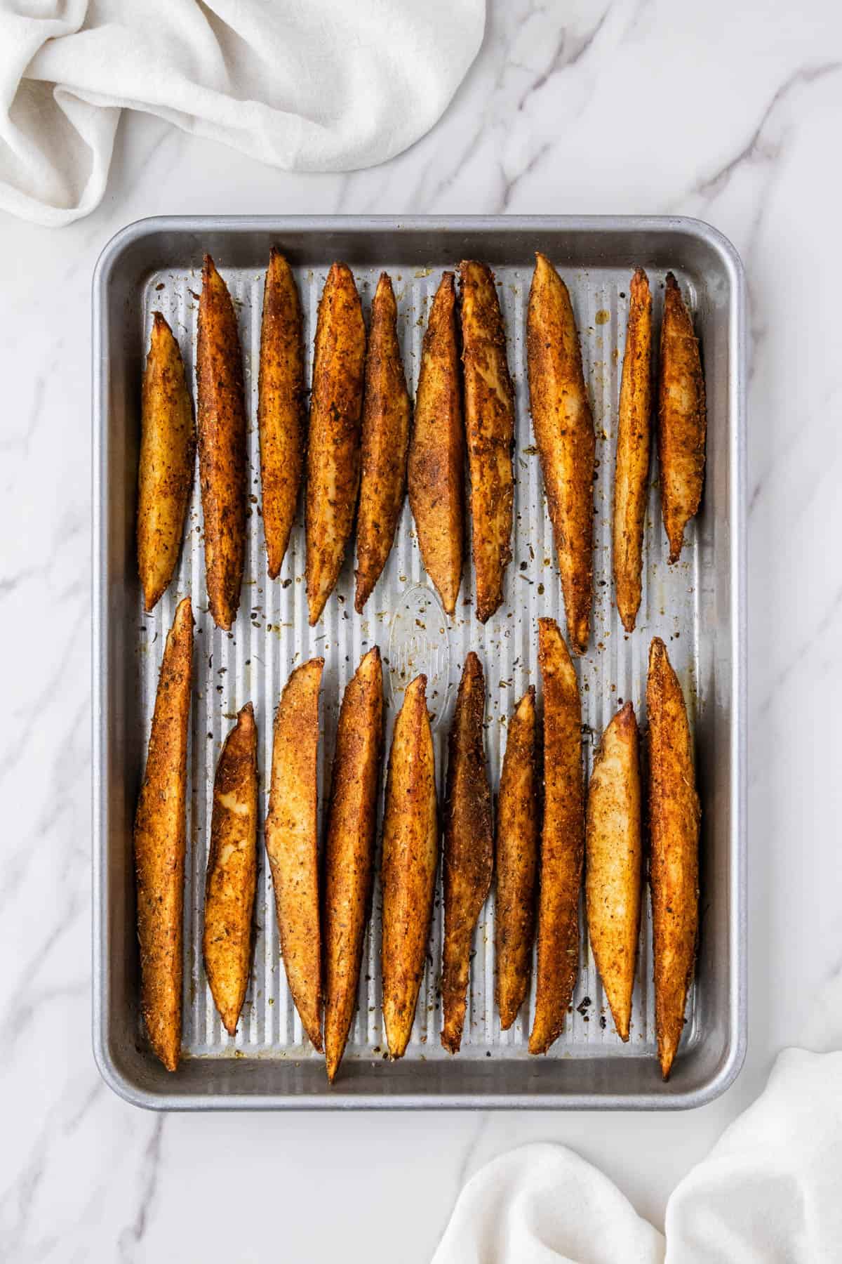 cooked potato wedges with seasoning with baking sheet