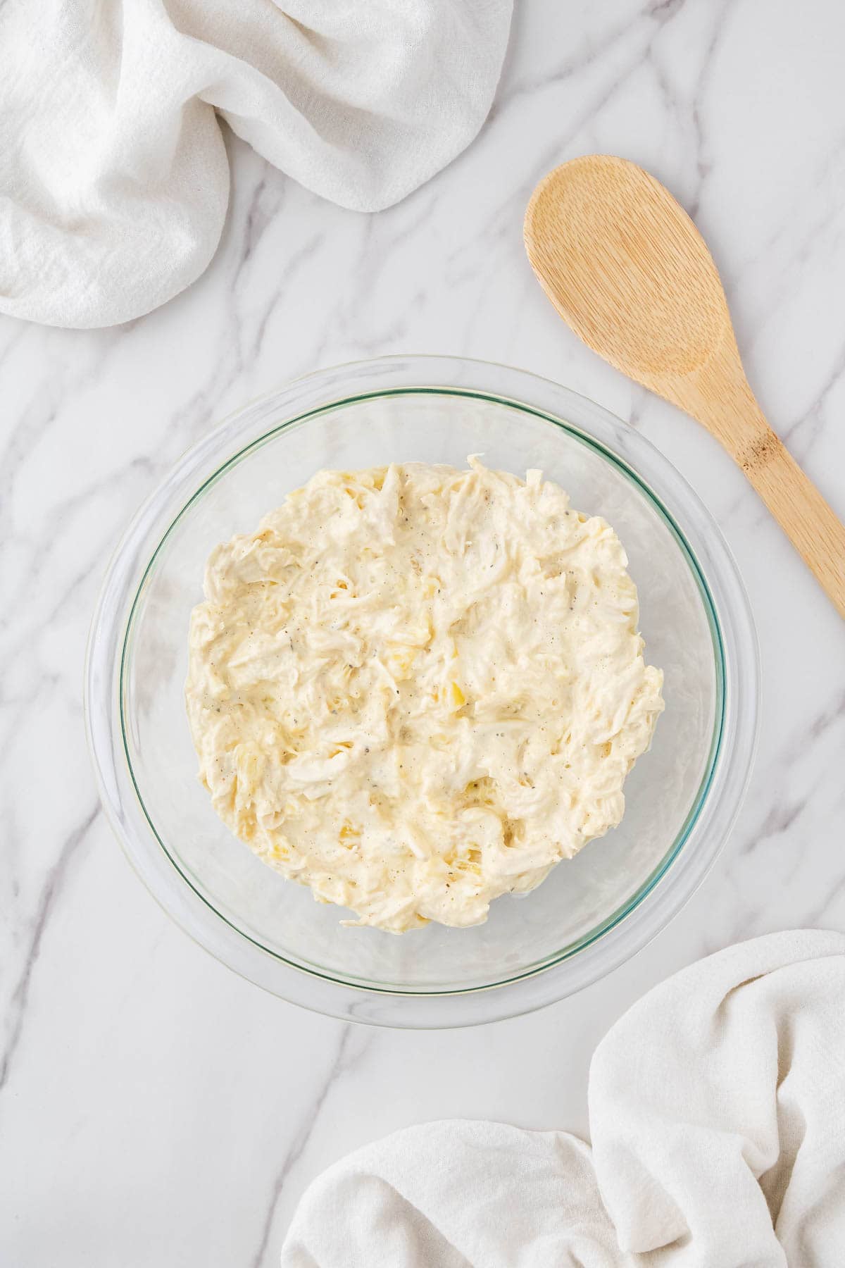 mixed ingredients in clear bowl with wooden spoon next to it