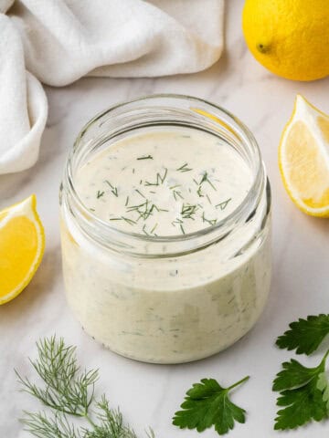 overhead view of jar of copycat texas roadhouse ranch with herbs and lemon slices in the back