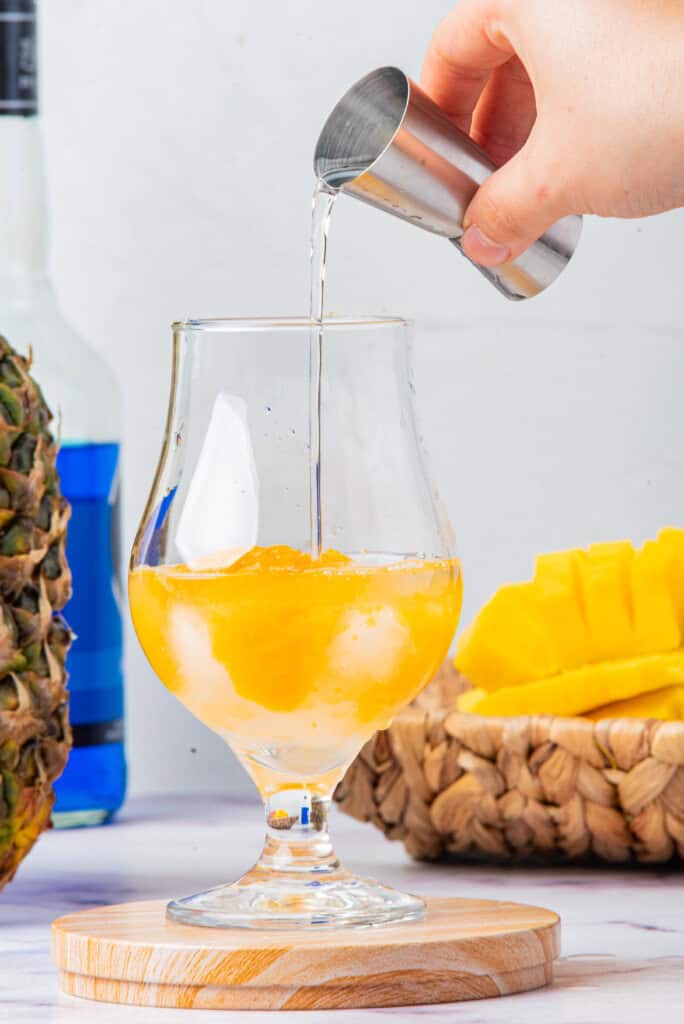 Clear spirits being poured over mango layer for Cheddar’s Island Tiki Cocktail