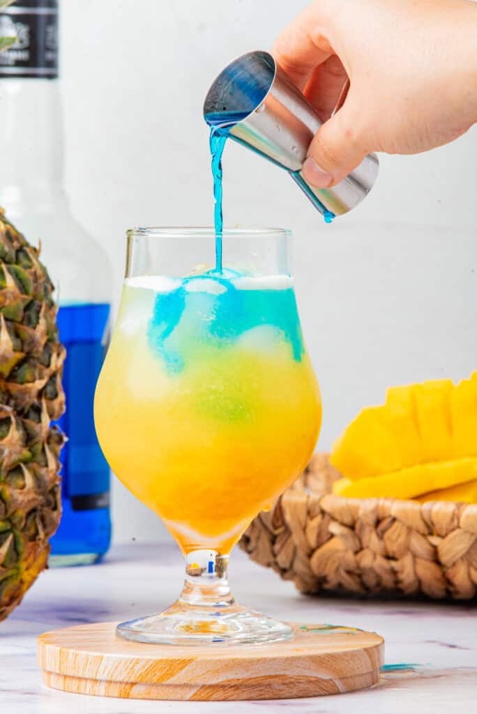 Blue curaçao being poured to create layers in Cheddar’s Island Tiki Cocktail