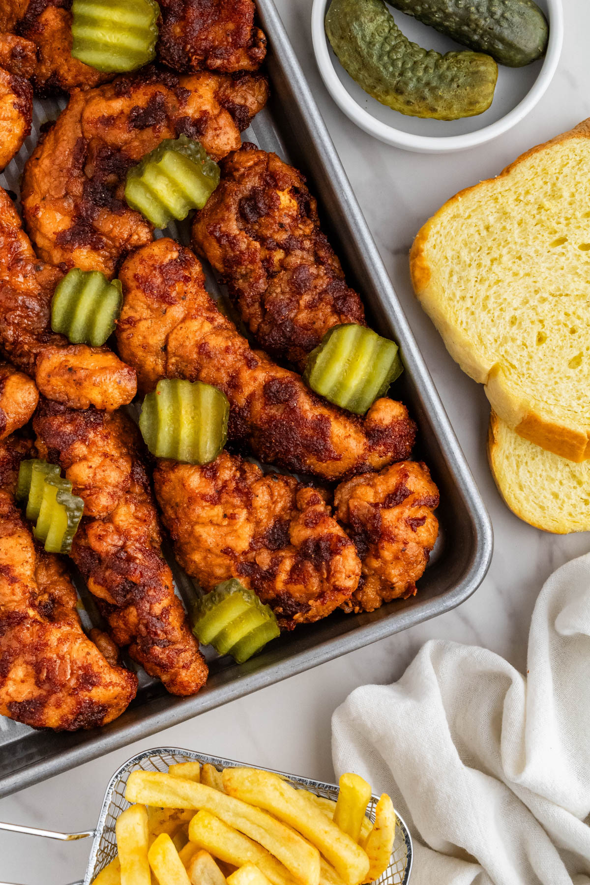 baking sheet with KFC Nashville hot chicken recipe with pickles on it with bread in background