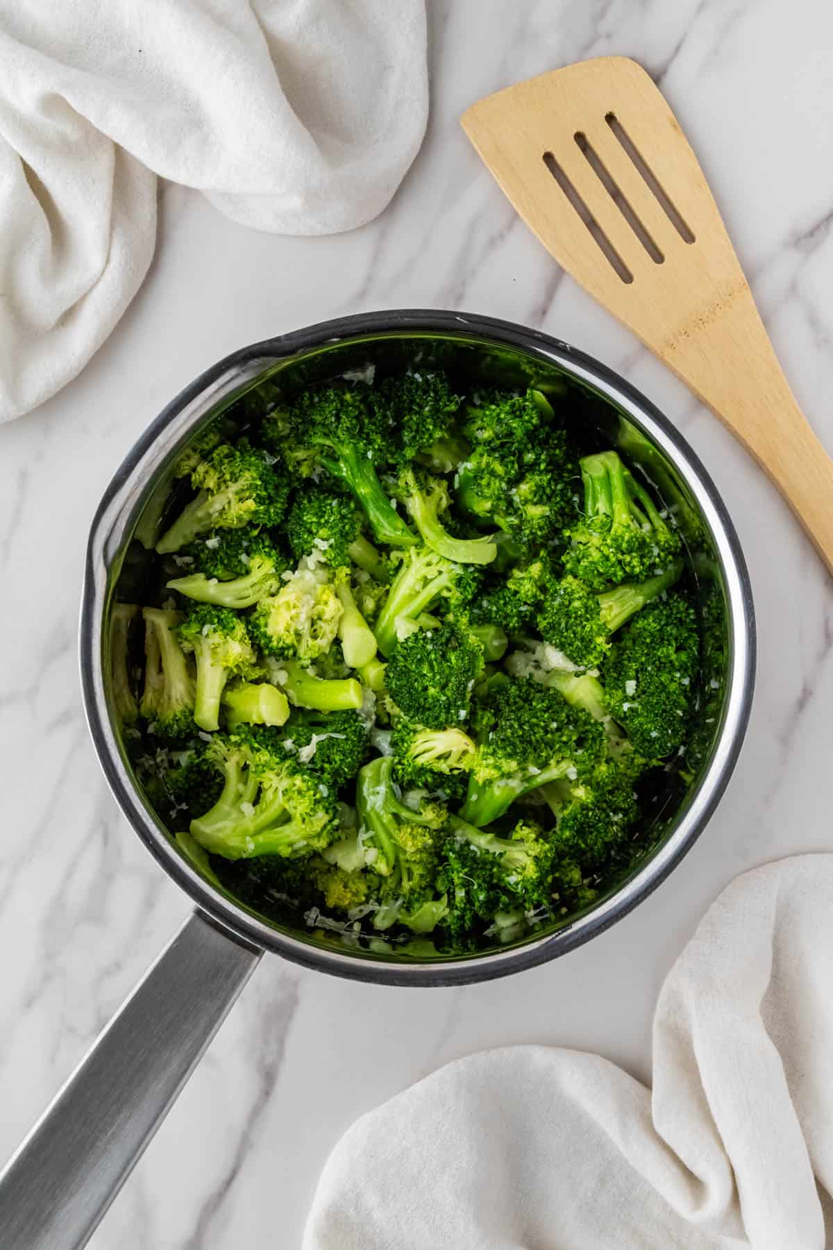 vibrant green veggies in saucepan with wooden spatula on side