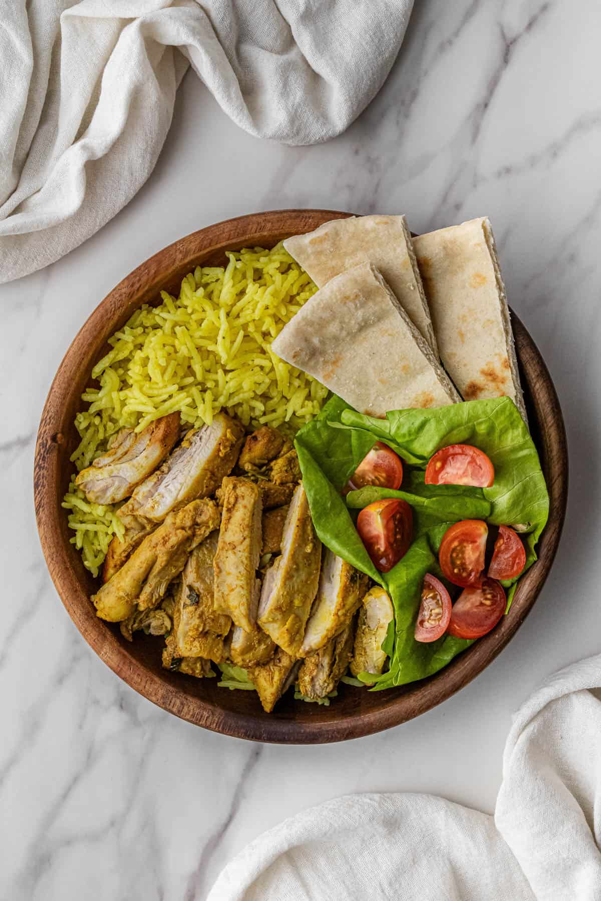 chicken, pita bread, and vegetables over rice in a bowl