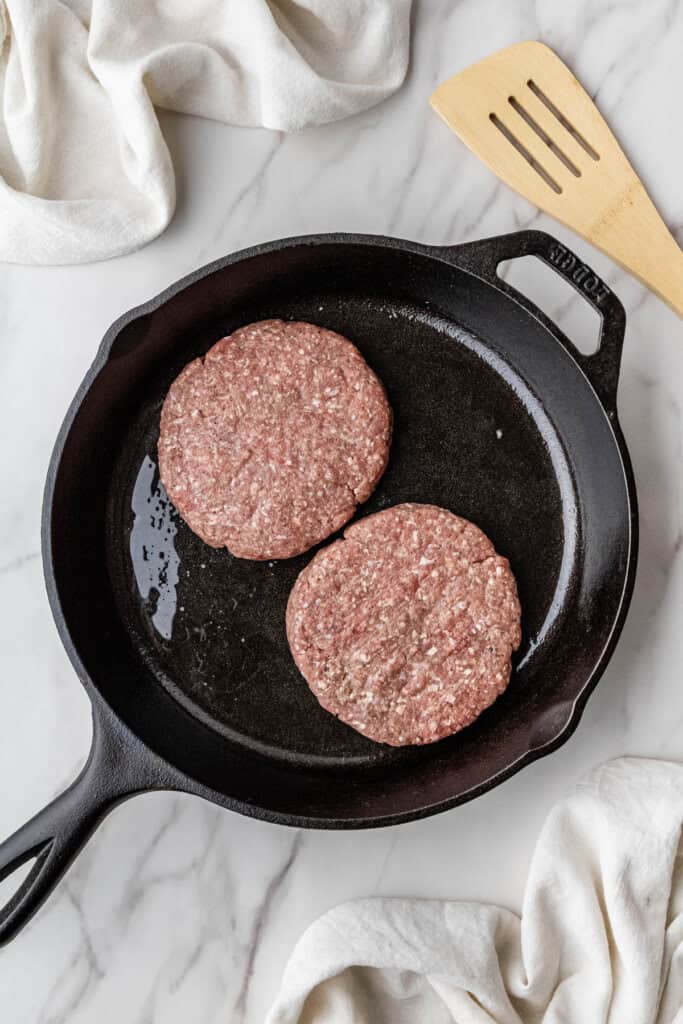two ground beef patties in a cast iron skillet