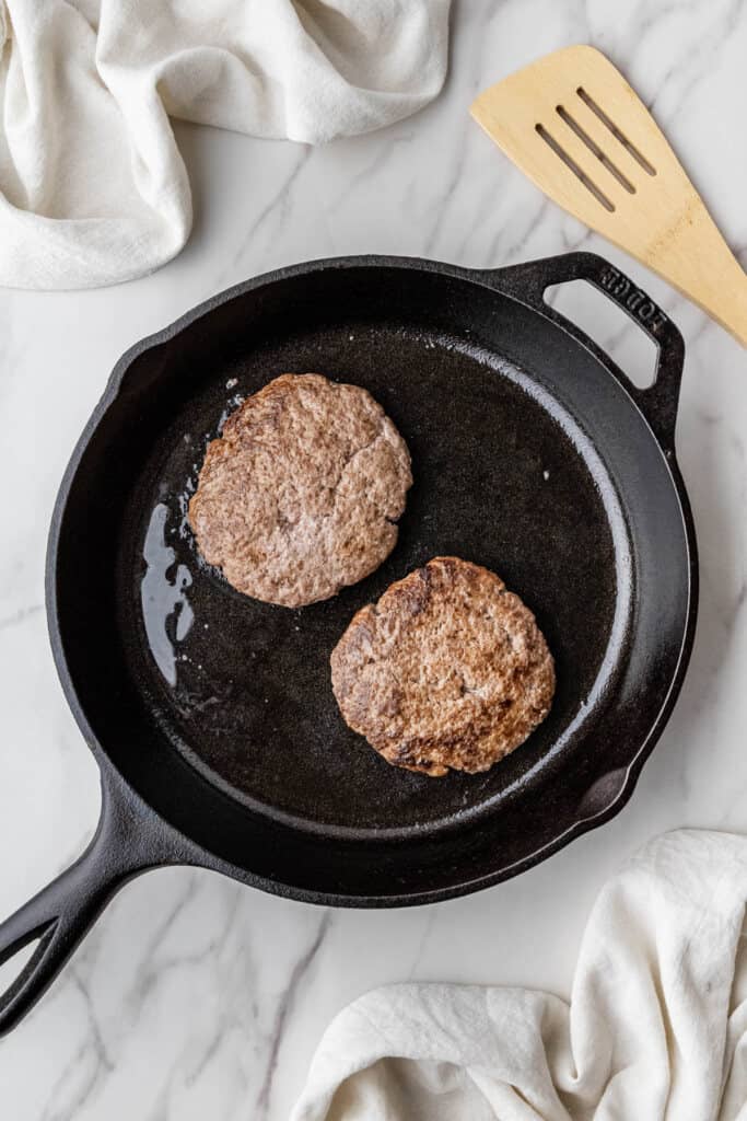 2 beef patties cooking in a cast iron skillet