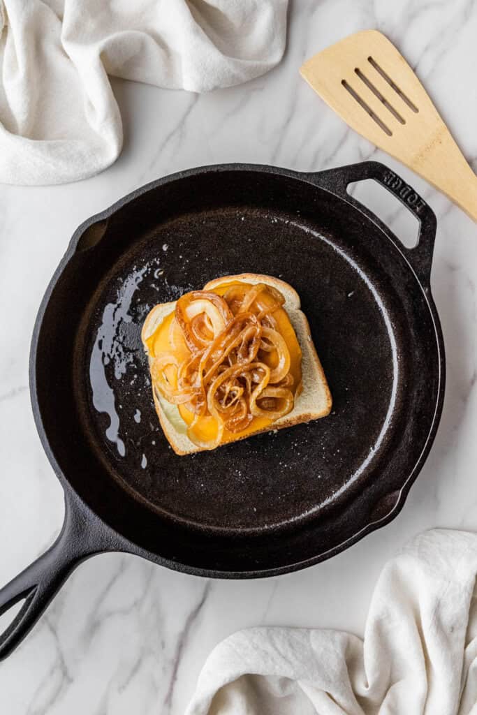 onions and burgers with cheese on a piece of toast in a cast iron skillet